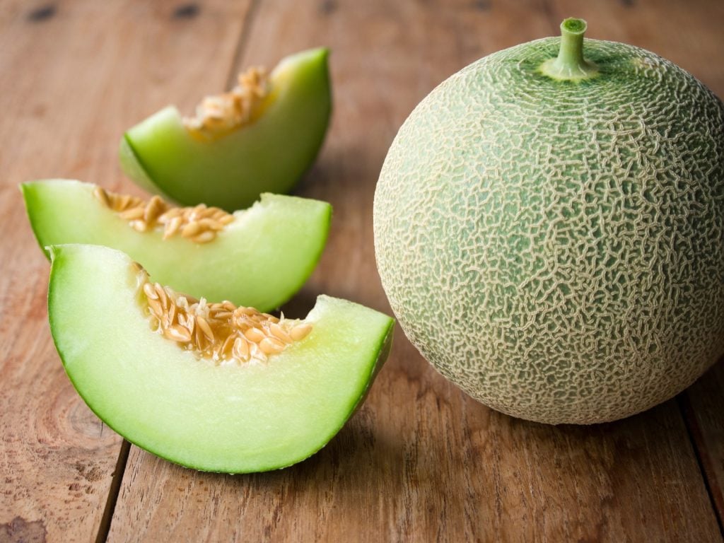 Fresh cut and whole honeydew melon on a rustic wooden table