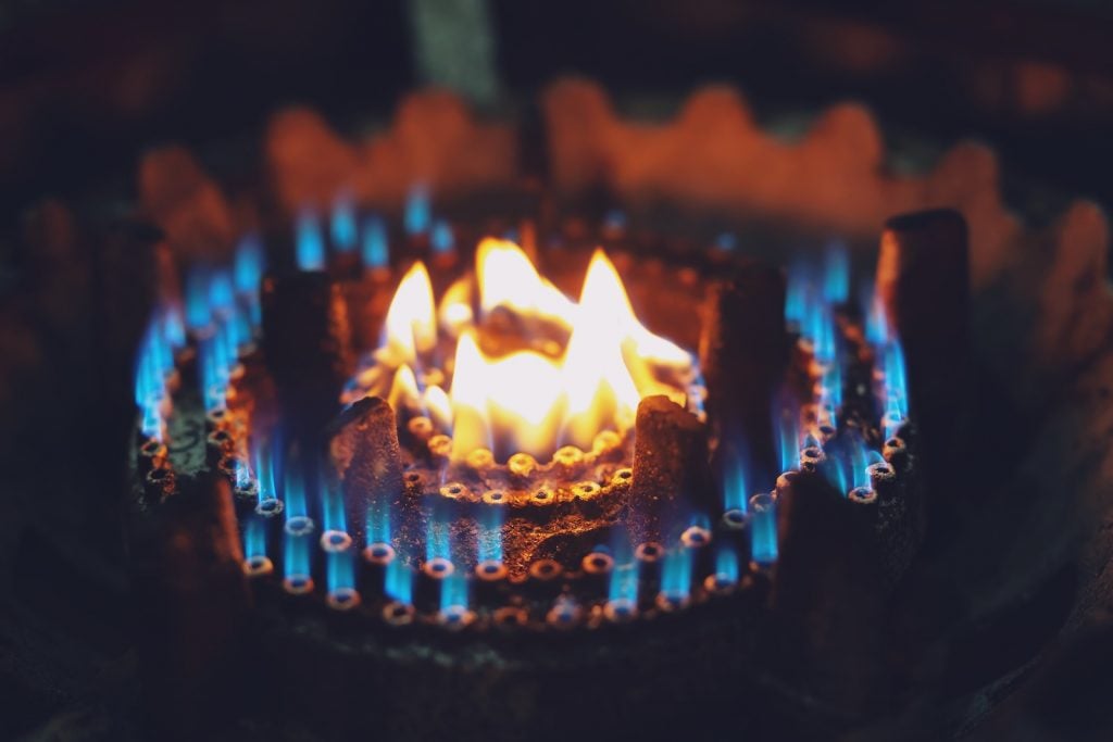 Burning gas stove burner hob with a light yellow flame and smaller blue flames surrounding it