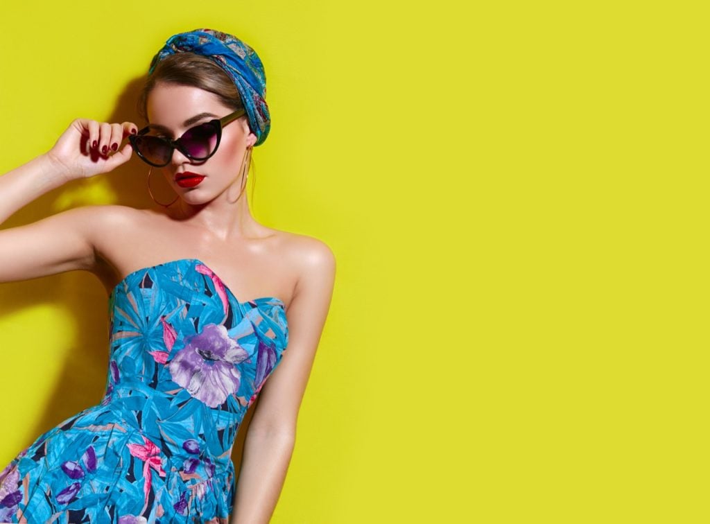 Girl in bright blue dress with headscarf and sunglasses in front of yellow wall