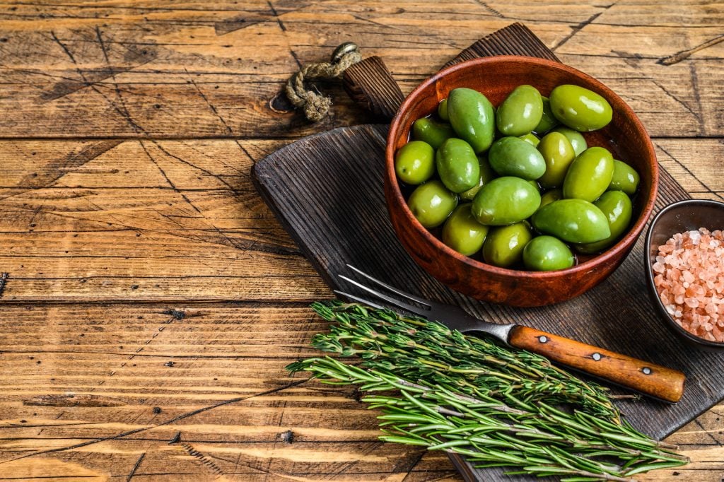 Marinated big green olives in dark wooden bowl with herbs and rosepink himalaya salt as decor