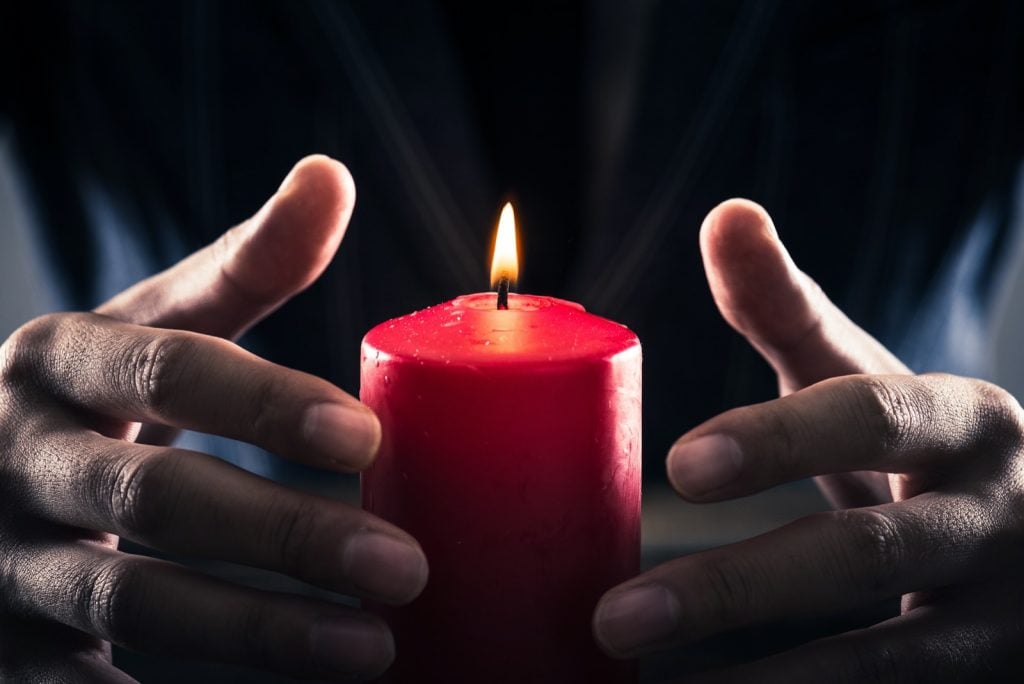 Practicing candle magic with hands placed around a burning red candle