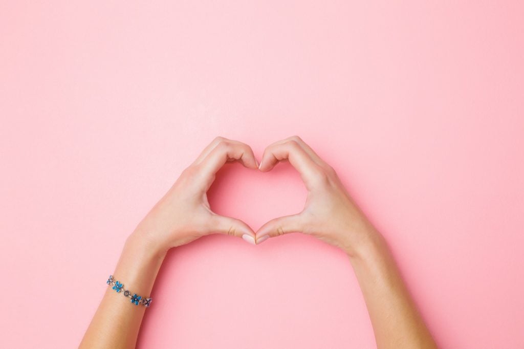 Heart shape created by woman's hands on a pink background