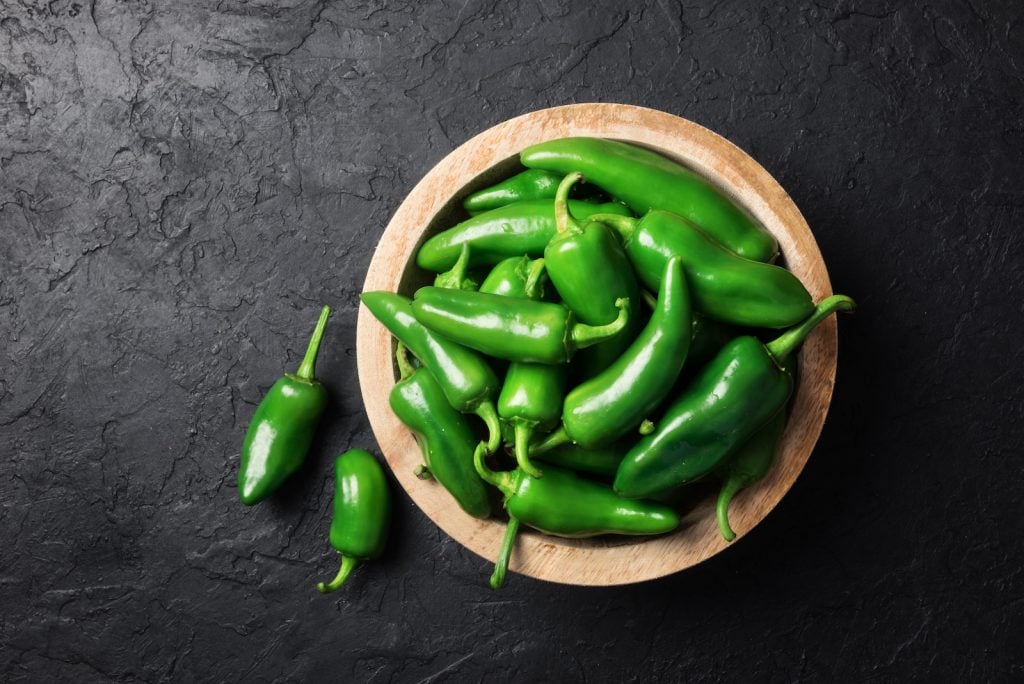 Green jalapeño peppers in a wooden bowle on black background