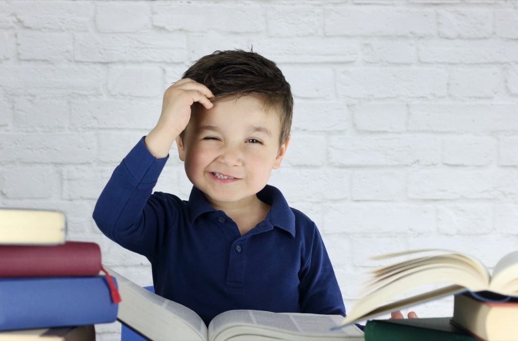 Kid surrounded by books scratching his head trying to learn how to read