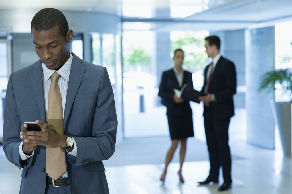 Man in grey suit looking at phone in office lobby after job interview
