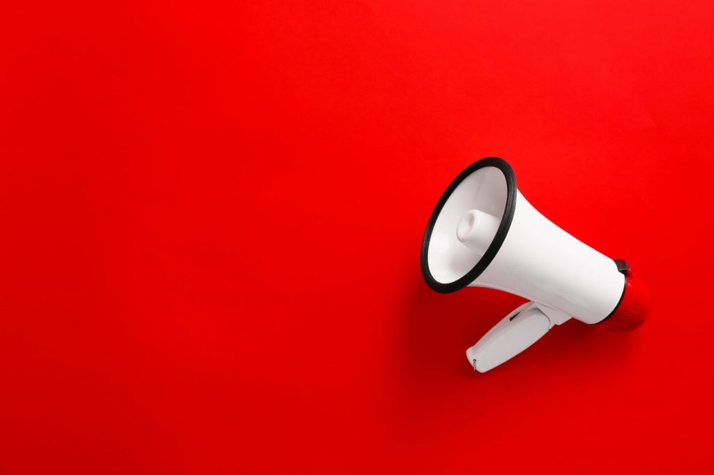 Modern megaphone calls for attention on red colored background