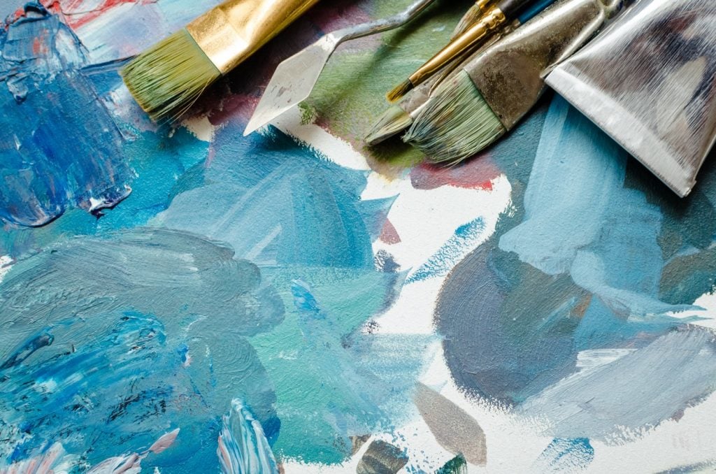 Paint brushes and oil paint tube on artist palette. Mixed turquoise colors and other cyan shades