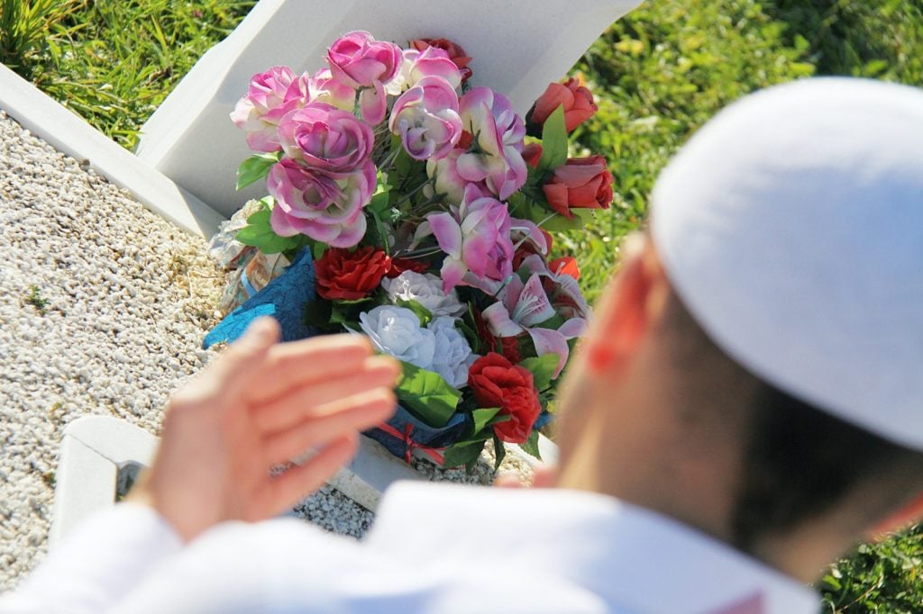 Pakistani man in white clothes praying in front of a gravestone