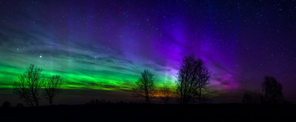 Panoramic photo of northern lights or aurora borealis in green, purple and orange colors