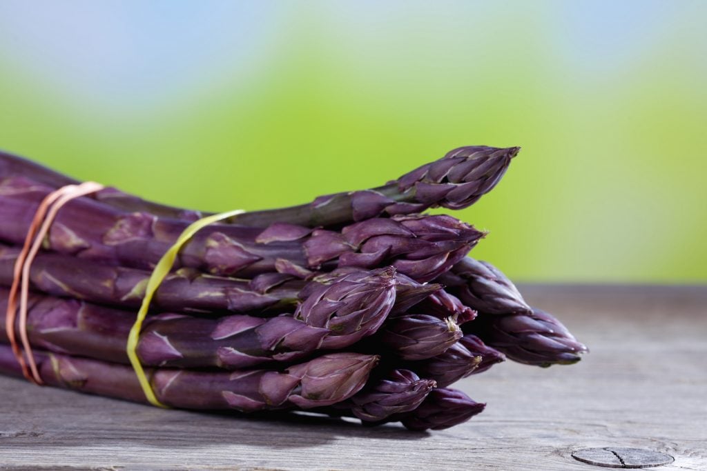 Closeup of a bundle of purple asparagus lying on a wooden table