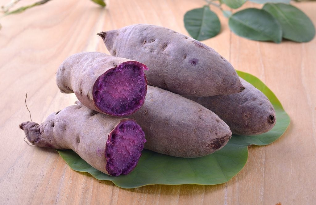 Purple yam also known as Ube lies in a stack on a big green leaf on a wooden table