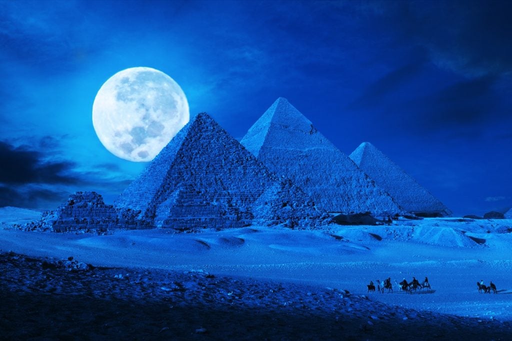 Pyramids in Egypt in a blue color lit up by the moonlight