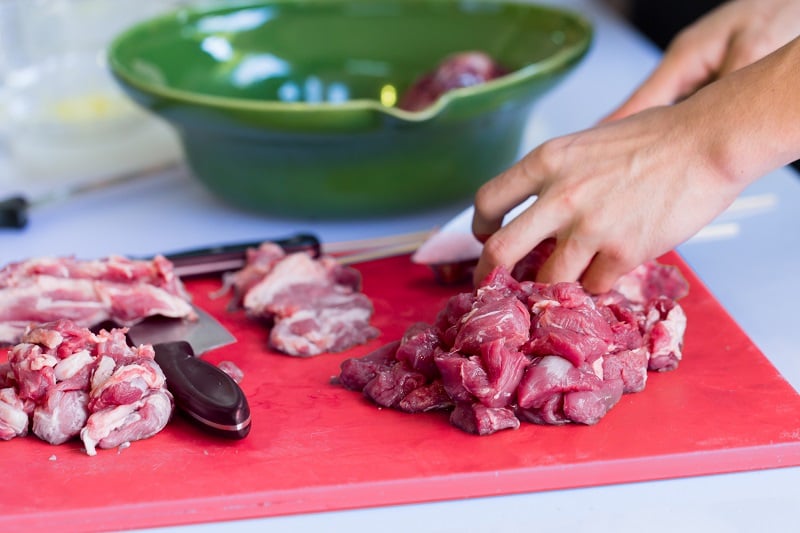 meat being chopped on a red colored chopping board