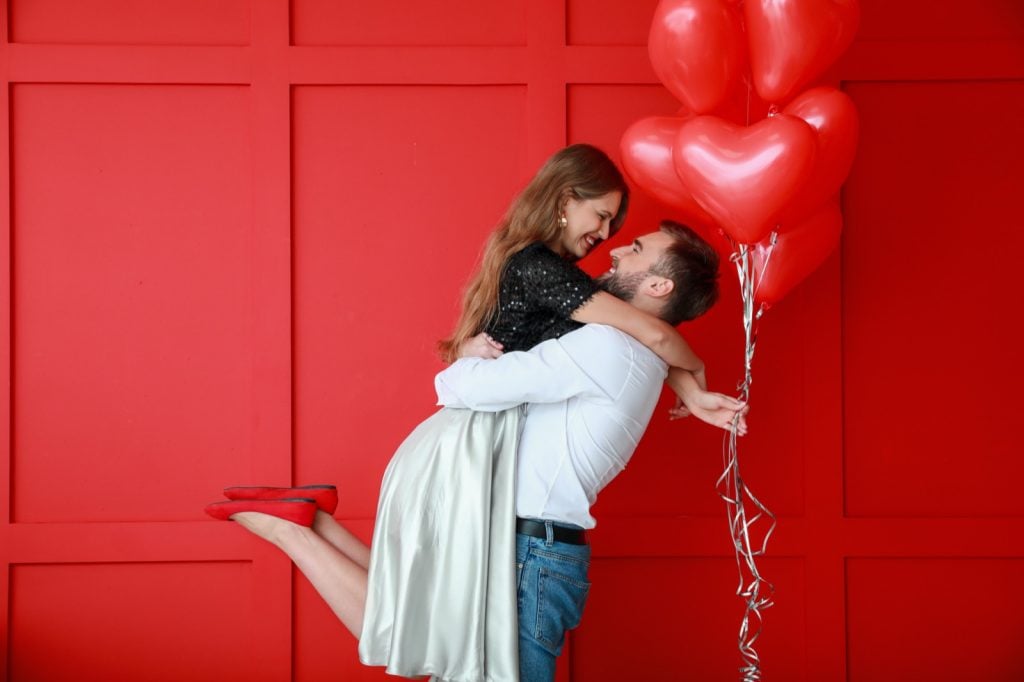 Happy couple with red heart-shaped balloons on colored background symbolizing passion and love