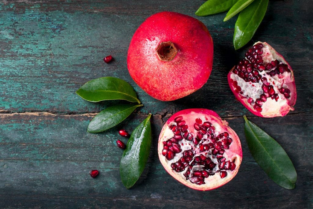 Whole and cut red pomegranate with leaves on wooden vintage background