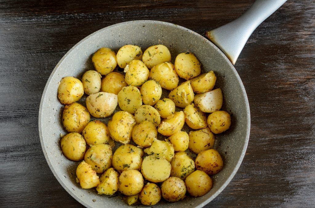 Roasted young potatoes in a pan with green herbs