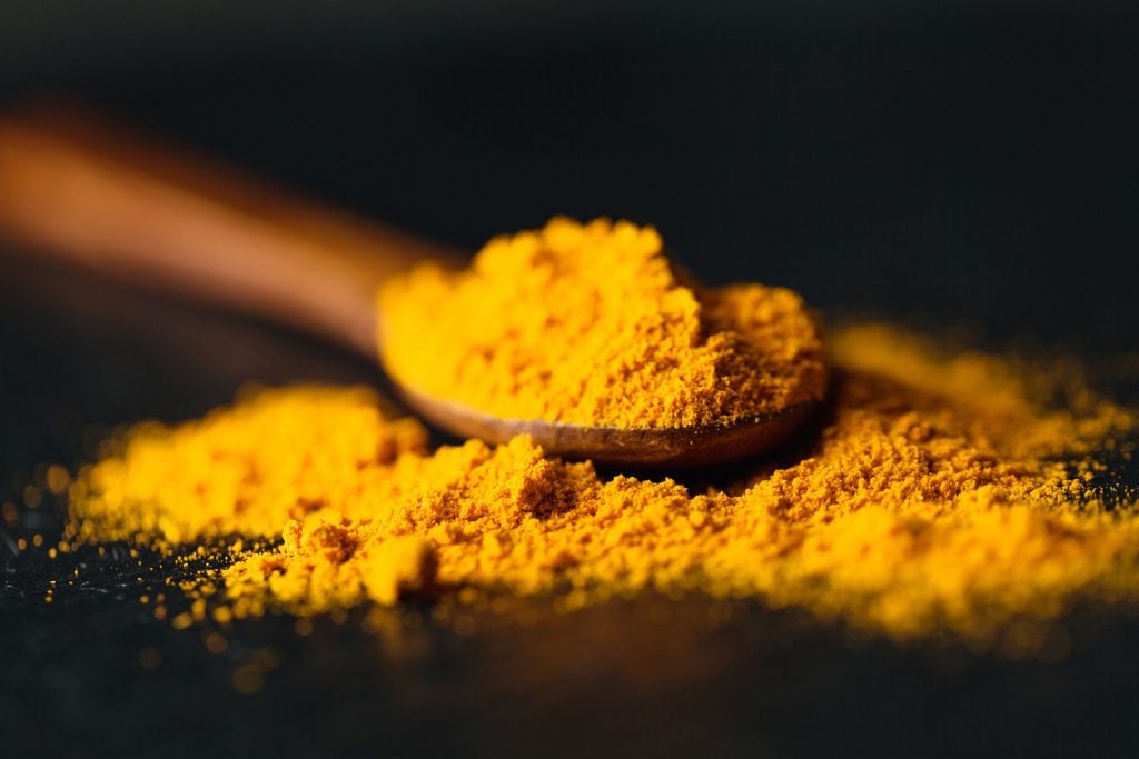 Saffron powder with yellow crocin pigment in a spoon on a dark background