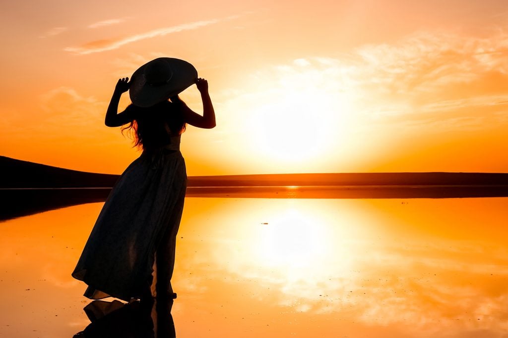 Silhouette of a woman in a dress standing on a lake looking out at the universe during a colorful sunset