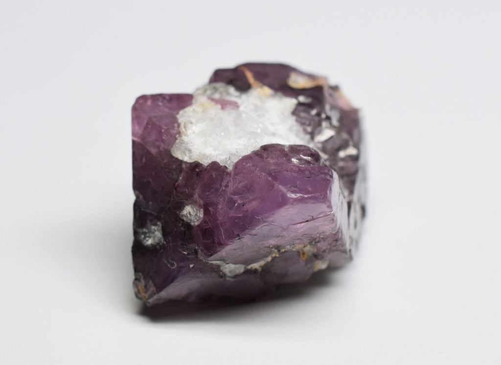Purple raw spinel stone lies on a grey background