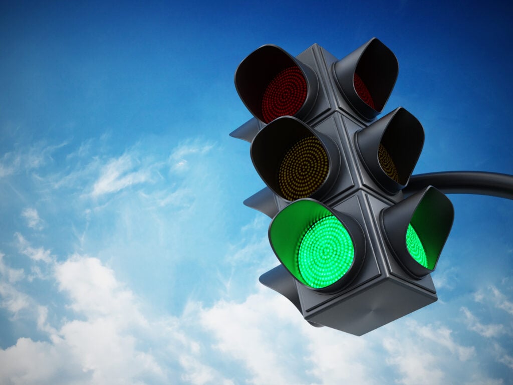Green traffic light against blue sky.