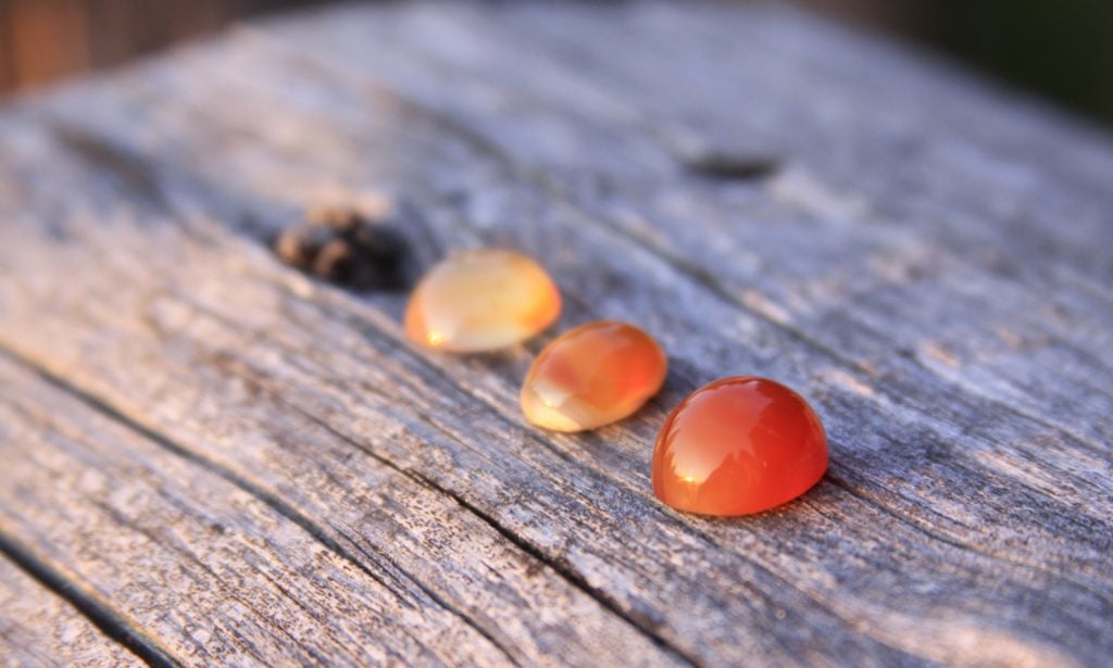 Three orange-red chalcedony agate gemstones on a wooden table