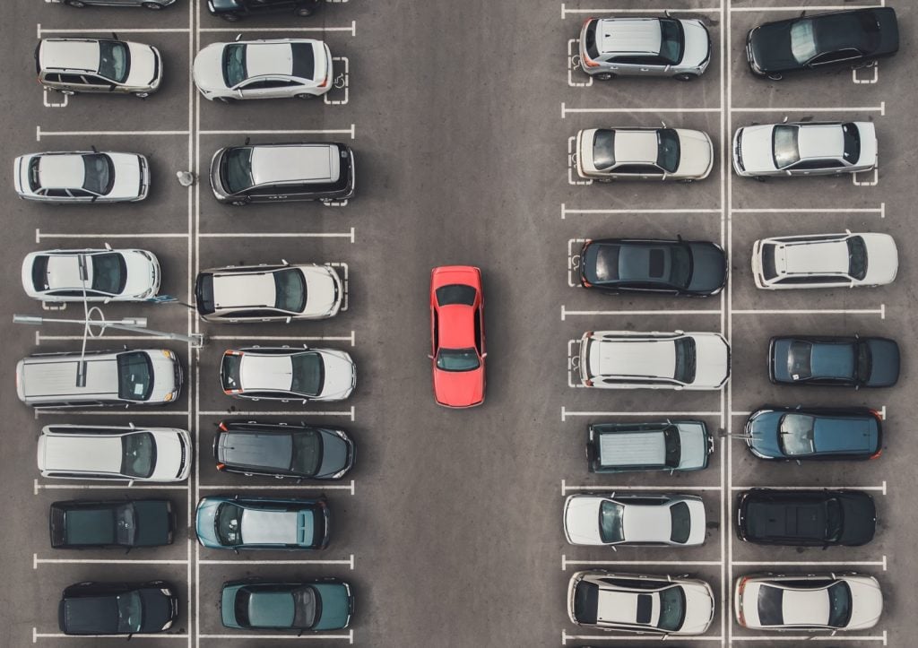  top view of crowded parking lot with bright red colored car among the grey of keskinkertaiset autot