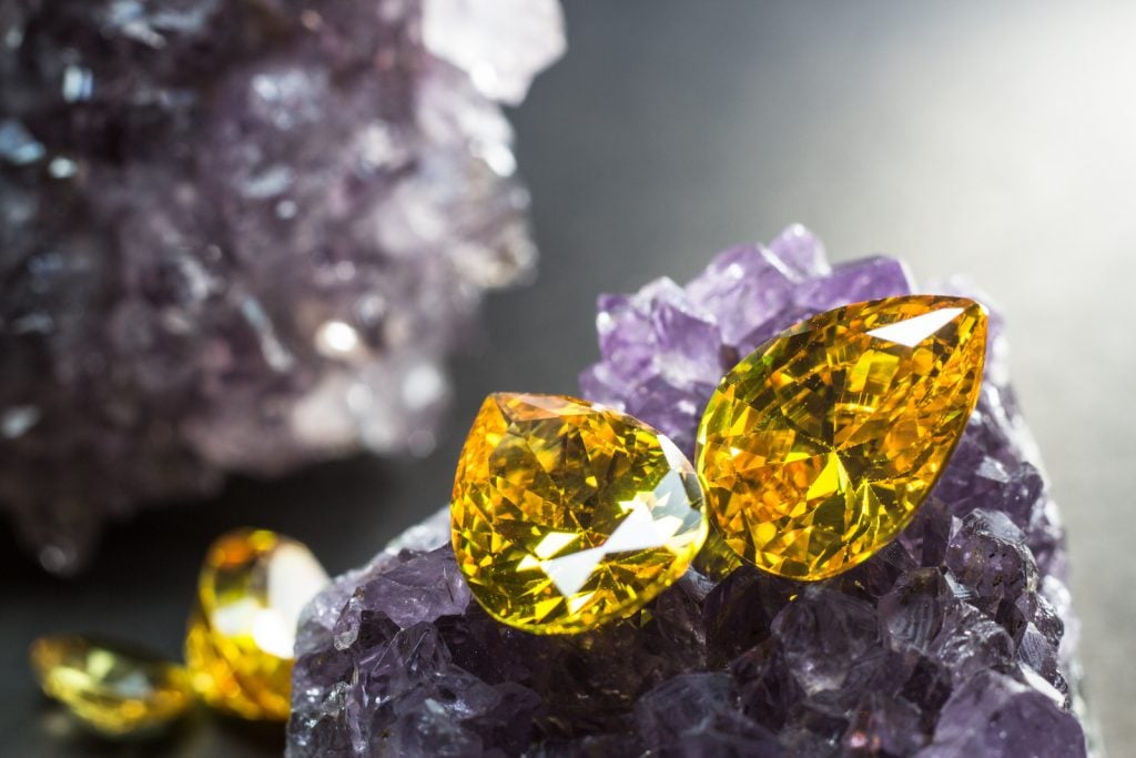 Two teardrop-shaped yellow sapphires resting on top of purple amethyst