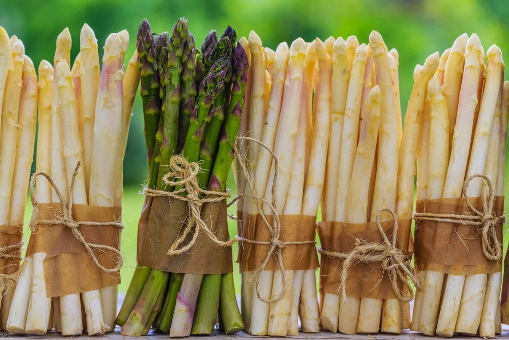 Bunches of white asparagus standing on a table with one green bunch of asparagus among the white