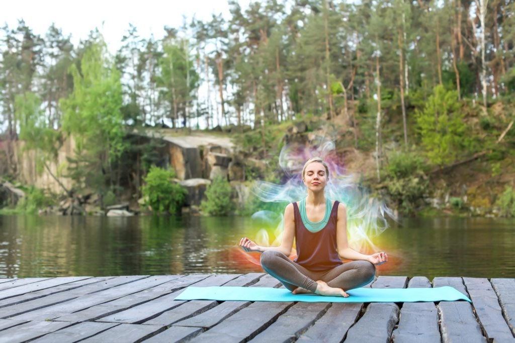 Woman sitting outdoors near river with aura colors around her body