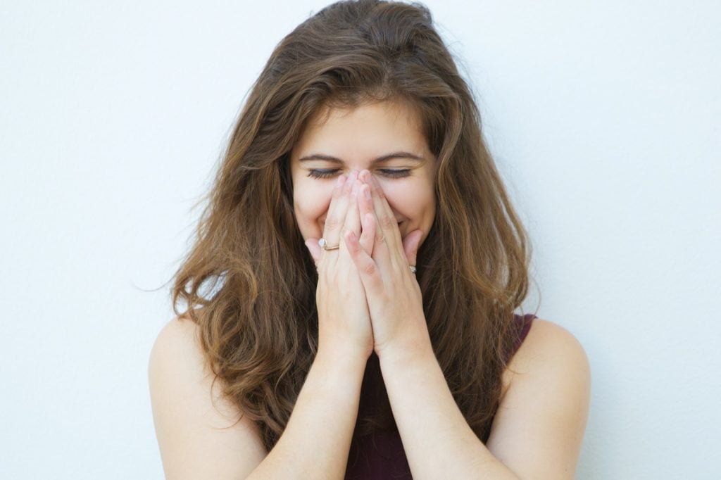 Woman laughing and covering her mouth with her hands