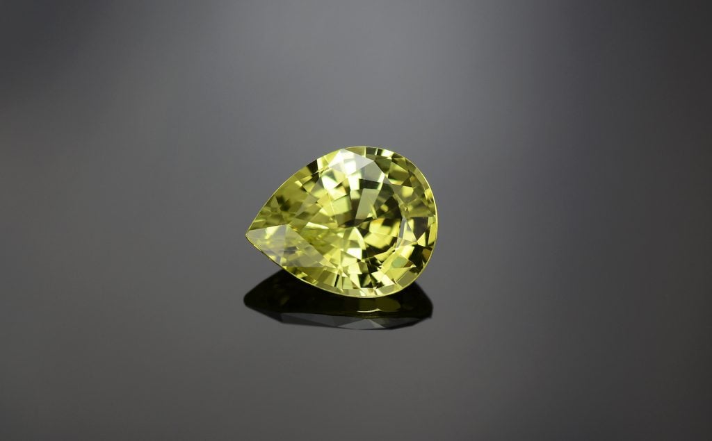 Natural bright lemon yellow color chrysoberyl, drop shaped faceted on grey background