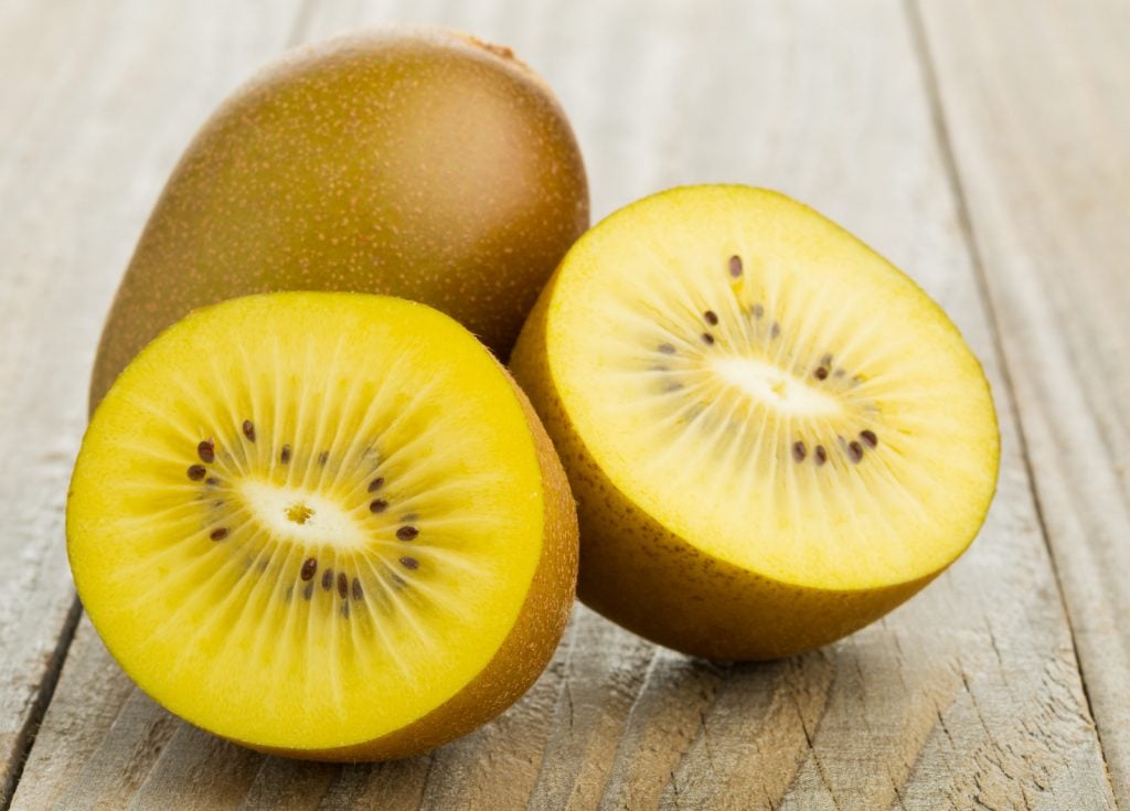 Whole and cut golden yellow kiwifruit on wooden cutting board