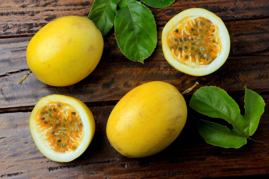 Yellow passion fruit with leaves and one passion fruit cut in half on rustic wooden table